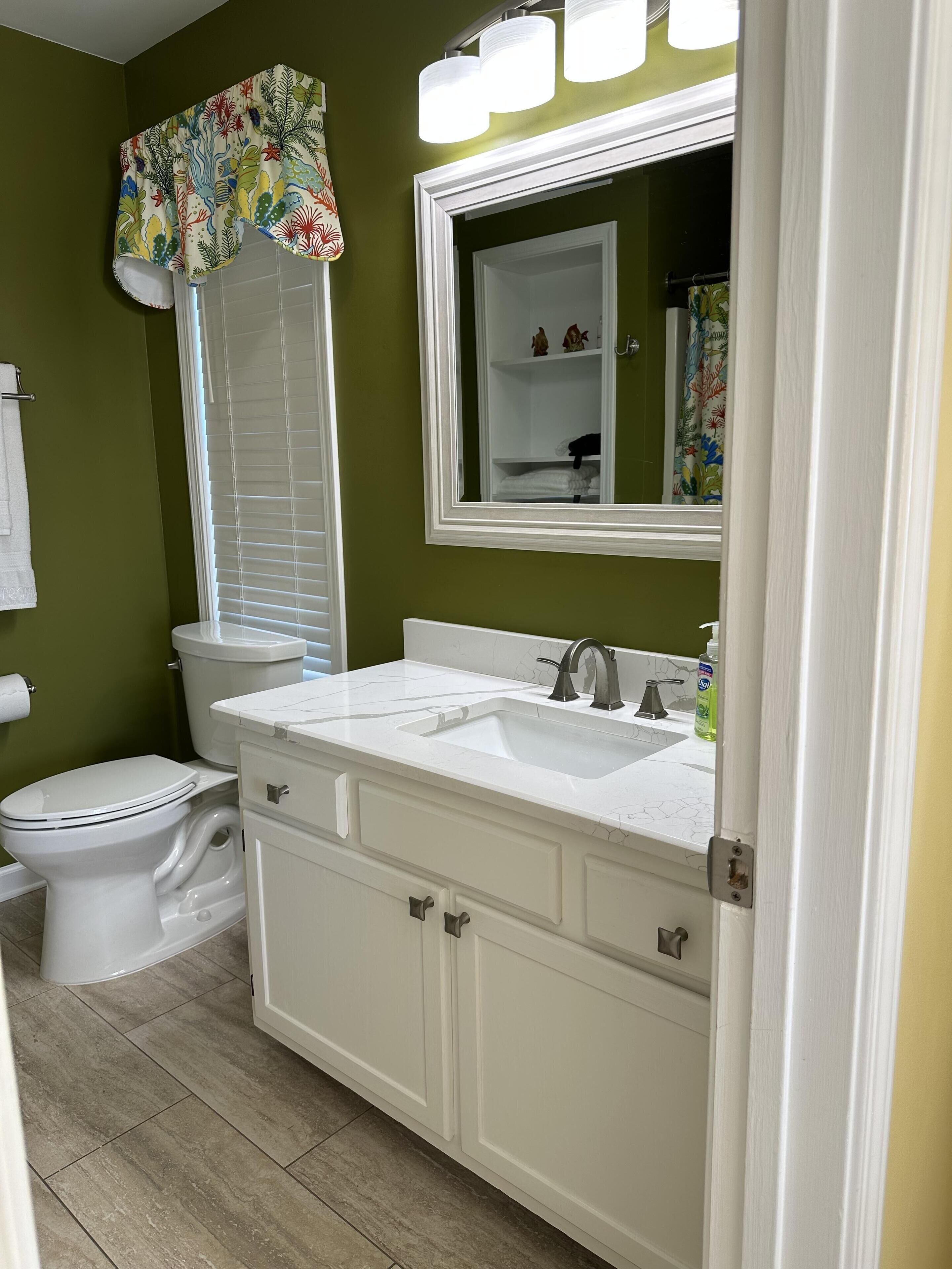Un baño con inodoro blanco, lavabo con espejo y cortina de ducha estampada con motivos florales.