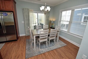 A kitchen with a stainless steel refrigerator, wooden cabinets, a dining table with chairs, a chandelier, and a window with blinds. - Just Beachin' - Second Row complex in Garden City Beach (Garden City)