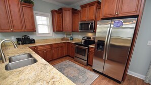 A kitchen with wooden cabinets, stainless steel appliances, granite countertops, and a built-in microwave. - Just Beachin' - Second Row complex in Garden City Beach (Garden City)
