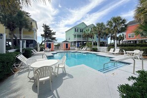 A swimming pool with lounge chairs and a table, surrounded by colorful buildings and palm trees. - Portofino II 315B - Oceanfront in Surfside Beach (Surfside Beach)