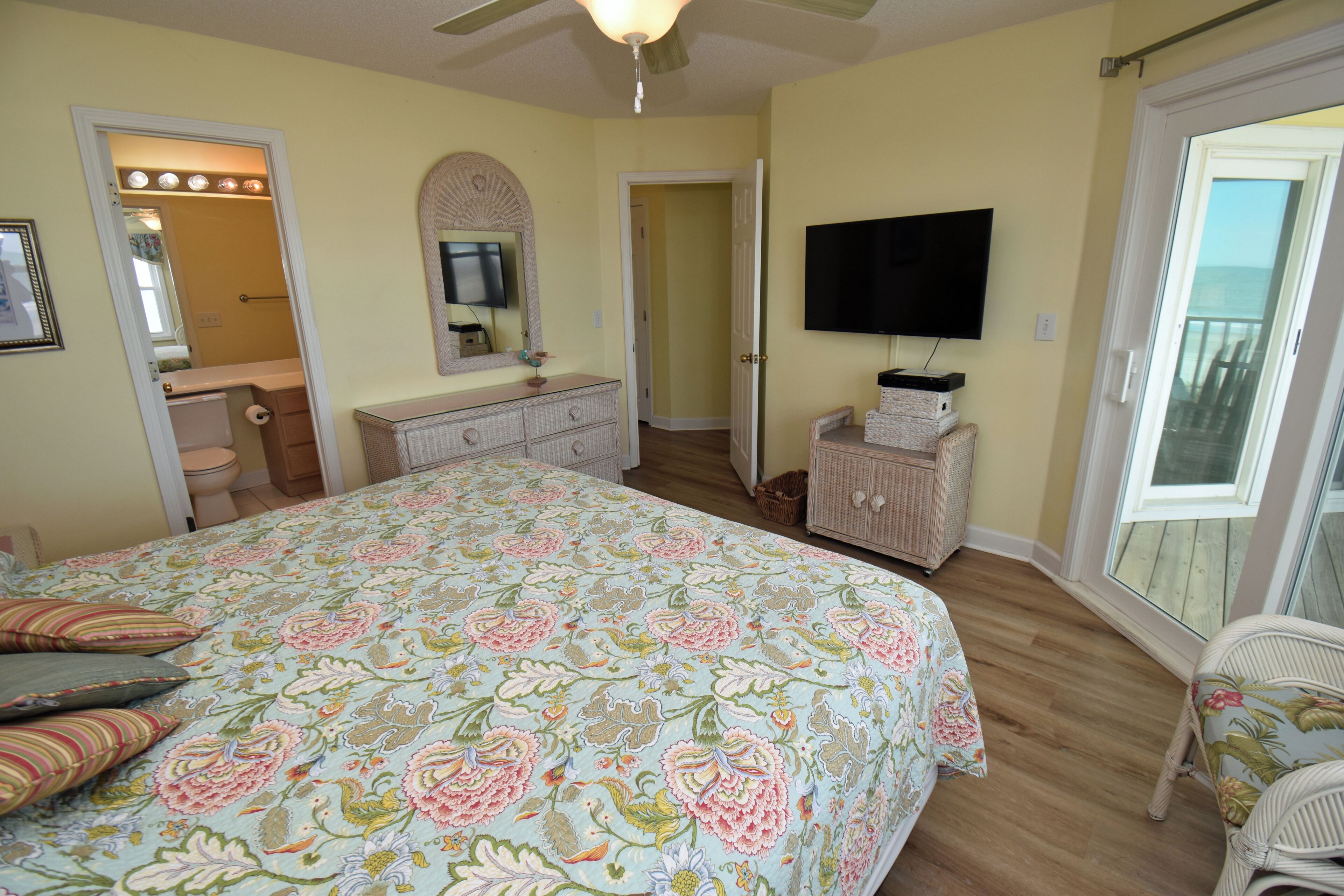 A bedroom with a bed, dresser, television, and a view through a door.