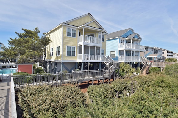 A beachfront property with multiple-story houses, a wooden deck, and a swimming pool.