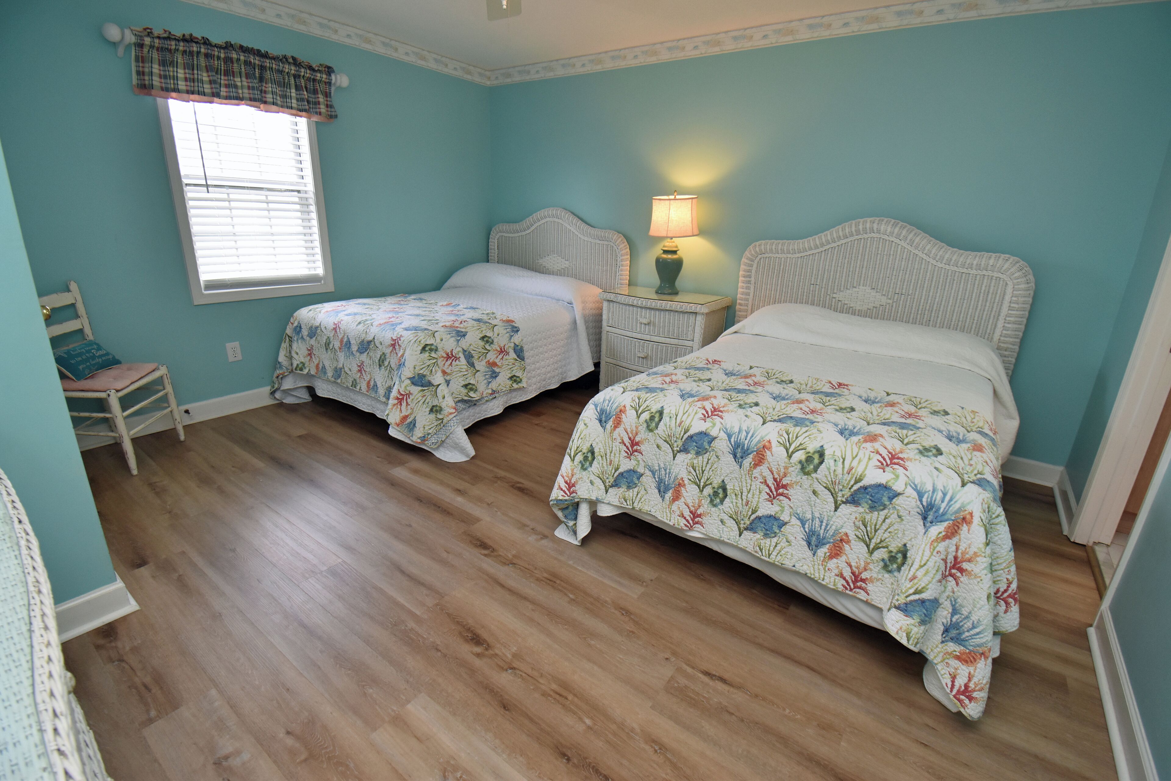 A bedroom with two beds, a nightstand with a lamp, a chair, and a window with blinds.