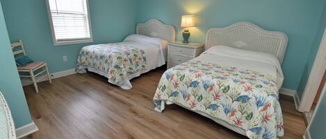 A bedroom with two beds, a nightstand with a lamp, a chair, and a window with blinds.