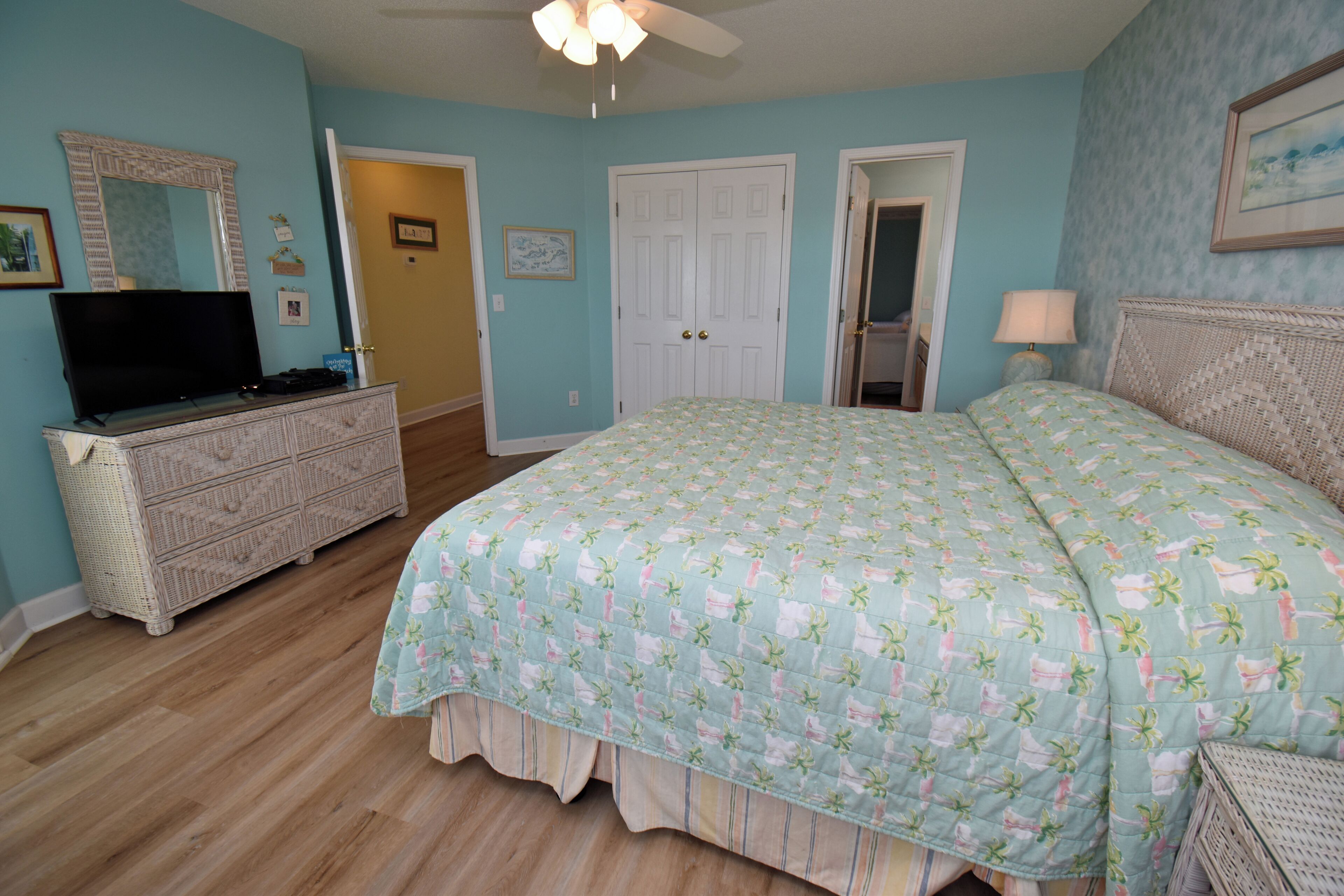 A bedroom with a bed, dresser, television, and a ceiling fan.