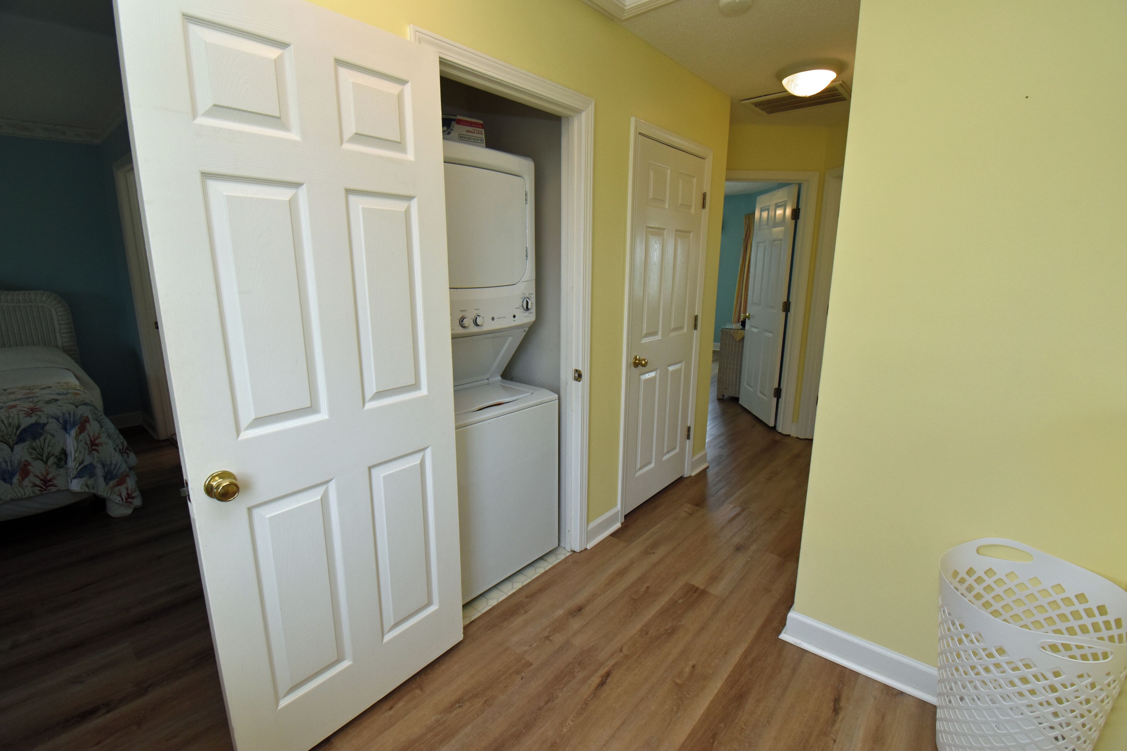 A hallway with wooden flooring, white doors, and a laundry area with a washing machine.