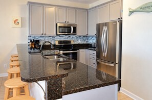 A modern kitchen with a granite countertop, stainless steel appliances, and a built-in island with stools.
