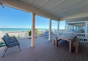 A covered outdoor area with a wooden deck, lounge chairs, and a view of the ocean.