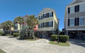 A residential area with multi-story houses, a clear sky, and a paved driveway.