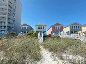 En rad strandhus med en sandstig som leder till entrén, omgivna av kustnära växtlighet.