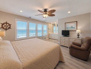 A bedroom with a large bed, a ceiling fan, a TV, and a view of the ocean through the windows. - Portofino IV 2002 - Oceanfront in Garden City Beach (Garden City)