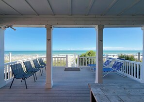 A covered deck with chairs and a view of the beach.