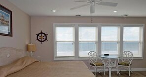Une chambre à coucher comprenant un lit, un ventilateur de plafond, une fenêtre avec des stores, une petite table avec des chaises et une boussole fixée au mur.