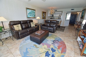 A living room with a brown leather sofa, a matching ottoman, a patterned rug, and a bookshelf with books. - One Ocean Place 909 - Oceanfront in Garden City Beach (Garden City)