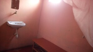 Un baño pequeño con un lavamanos blanco, un banco de madera y una única lámpara.
