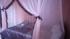 Una cama con unacolcha oscura y una almohada, bajo un dosel con cortinas translúcidas y un lazo en el centro.