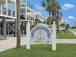 A sign for Portobello II with an anchor symbol, surrounded by residential buildings and palm trees.