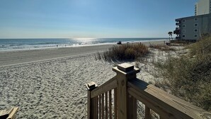 Une plage avec une promenade en bois qui mène à un bâtiment à étages doté de balcons.