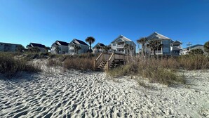 Une propriété située en bord de mer, comprenant plusieurs maisons, une plage de sable et un ciel bleu dégagé.