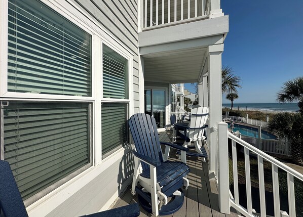 Een balkon met uitzicht op de oceaan, een zwembad en een eethoek met stoelen en een tafel.