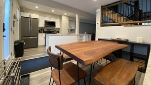 Una cocina moderna con armarios blancos, un refrigerador de acero inoxidable y un microondas integrado. En primer plano, se observa una mesa de madera con bancos.