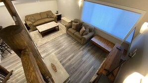 Un salón amplio con un ventanal grande, un sofá, una mesa de centro y un revestimiento de madera.