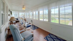 Quarto com vista para o exterior, ventoinha no teto e área de estar com cadeiras e mesa.