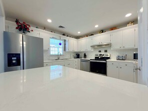 A modern kitchen with white cabinetry, stainless steel appliances, and a marble countertop. - Suit Up - Walk to Beach (Channelfront) in Garden City Beach (Garden City)