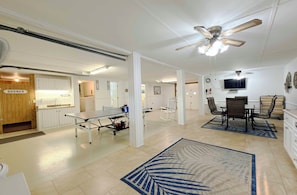 A spacious living area with a ping pong table, a television, and a ceiling fan. - Suit Up - Walk to Beach (Channelfront) in Garden City Beach (Garden City)