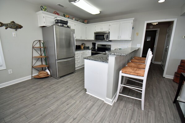 A modern kitchen with white cabinets, stainless steel appliances, and a wooden floor. - Portofino I 1428 - Oceanfront in Garden City Beach (Garden City)