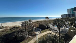 A beachfront view with a sandy beach, palm trees, and a pool area. - Portofino I 1428 - Oceanfront in Garden City Beach (Garden City)