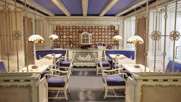 Un comedor con mobiliario blanco ornamentado, sillas tapizadas de púrpura y paneles decorativos en la pared.
