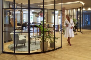 Ein modernes Interieur mit einer Glastrennwand, Holzboden und einem Essbereich mit Stühlen und Tischen.