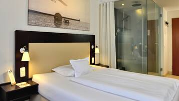 Una camera d'albergo con un letto grande, due abat-jour, un comodino, una cabina doccia in vetro e un'opera d'arte appesa al muro.