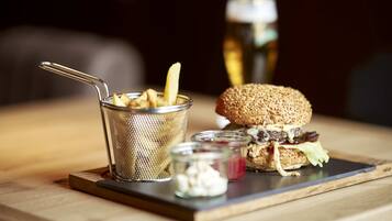 Een maaltijd met een hamburger, friet en een drankje op een houten tafel.