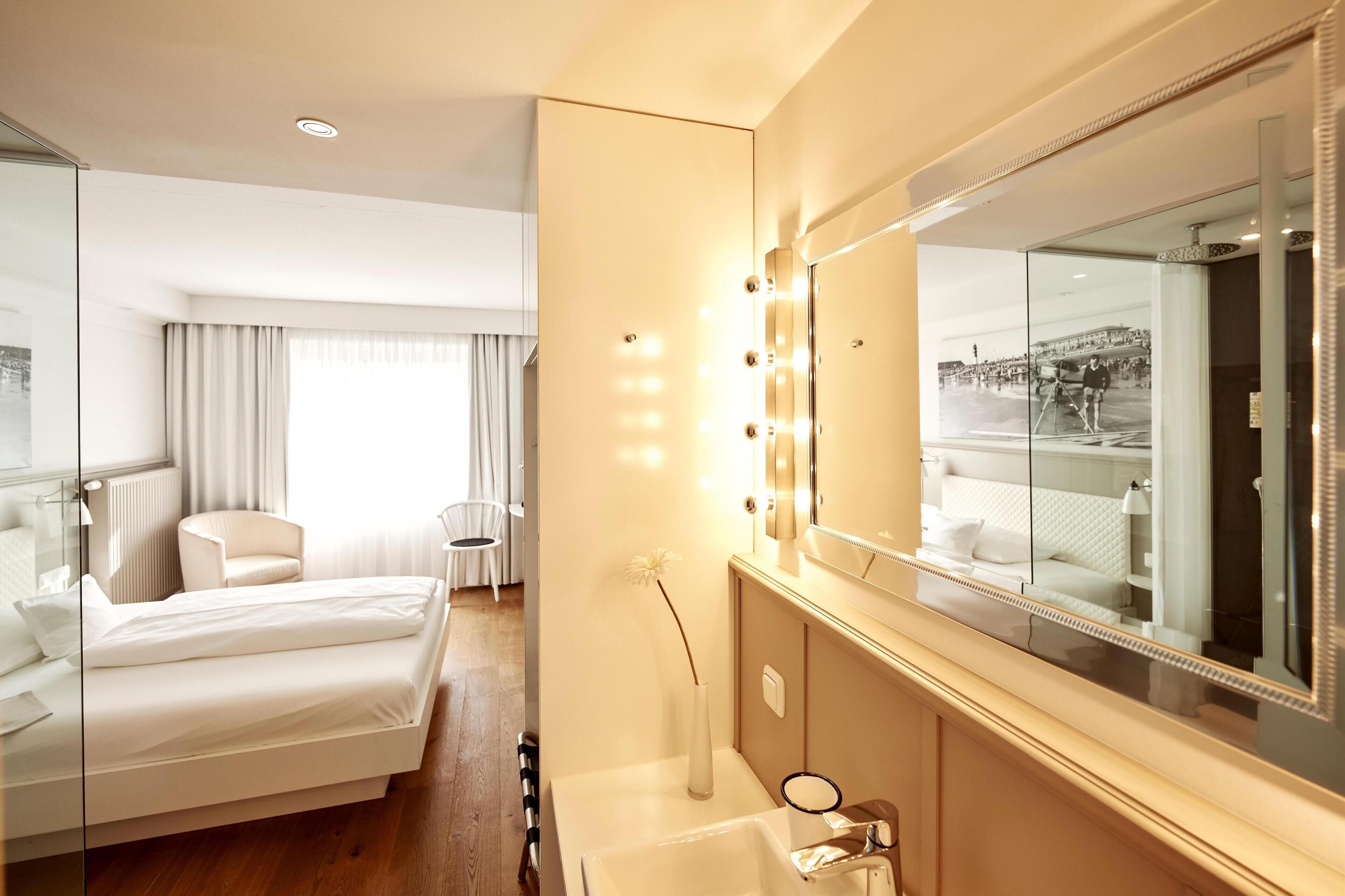 A hotel room with a bed, a vanity with a mirror, and a window with curtains.
