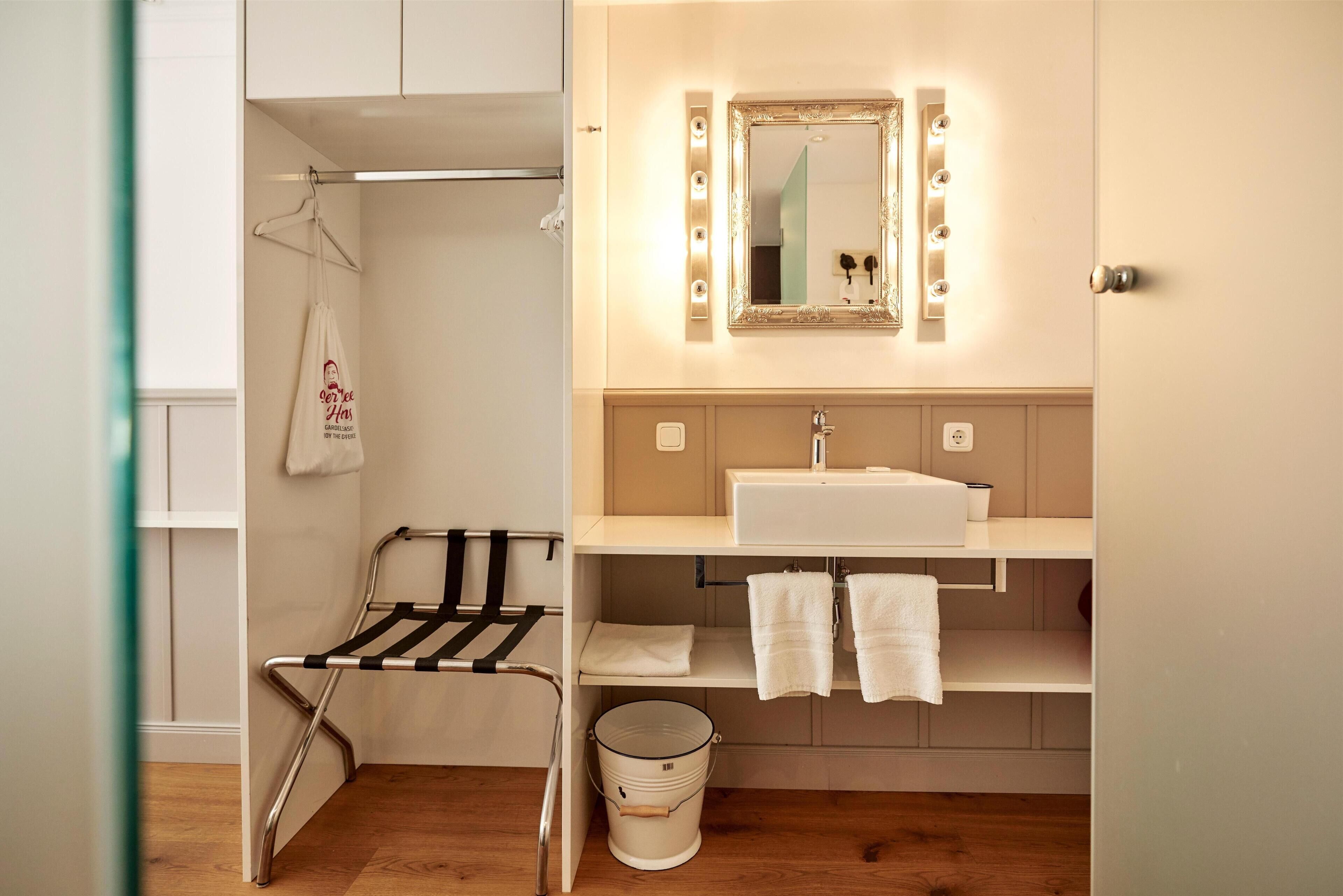 Ein Badezimmer mit Waschtisch, Spiegel mit Beleuchtung, Handtuchhalter und Wäscheständer.