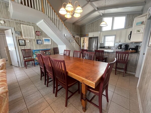A spacious dining area with a large wooden table and chairs, a kitchen with white cabinets, and a staircase leading to an upper level. - Vitamin Sea - Oceanfront in Surfside Beach (Surfside Beach)