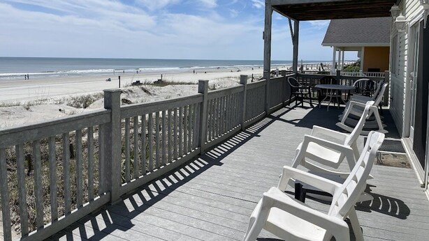 Une terrasse en bois avec des chaises blanches donnant sur une plage.