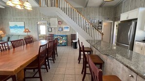 Un vaste espace de salle à manger avec une longue table et des chaises en bois, une cuisine dotée de plans de travail en granit et un escalier menant à un niveau supérieur.