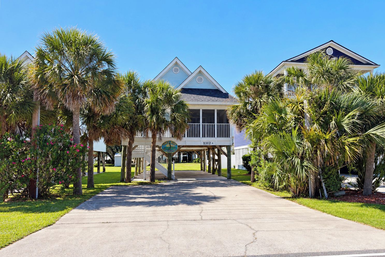 A beachfront property with a covered walkway leading to a building, palm trees, and a clear sky.