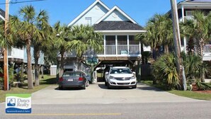 A two-story house with a covered garage, surrounded by palm trees. - Pebble Beach - Second Row in Surfside Beach (Surfside Beach)