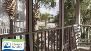 A room with a view of palm trees and a beach. There is a chair and a sign for Dunes Realty Vacation Rentals & Sales. - Pebble Beach - Second Row in Surfside Beach (Surfside Beach)