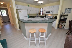 A kitchen with white cabinets, a granite countertop, and two wooden stools. - Pebble Beach - Second Row in Surfside Beach (Surfside Beach)