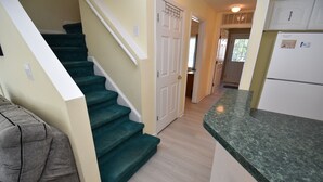 A kitchen with a green countertop, a white refrigerator, and a staircase with teal carpet. - Pebble Beach - Second Row in Surfside Beach (Surfside Beach)