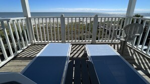 Une terrasse couverte avec des rampes blanches, deux chaises longues et une vue sur l’océan.