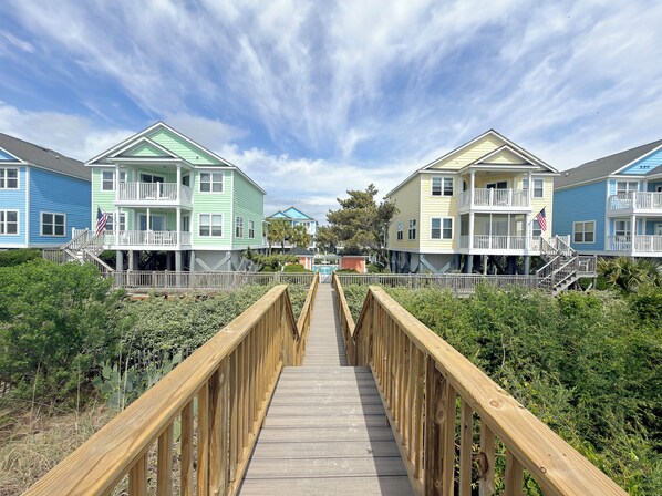 A wooden boardwalk leading to a row of colorful beach houses with balconies and railings.