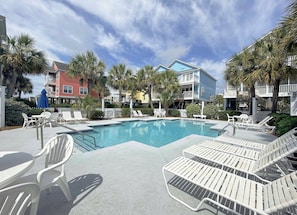 A pool area with lounge chairs, a pool, and buildings in the background.