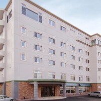 Un hotel de varios pisos con fachada plana, una entrada central y un estacionamiento visible.