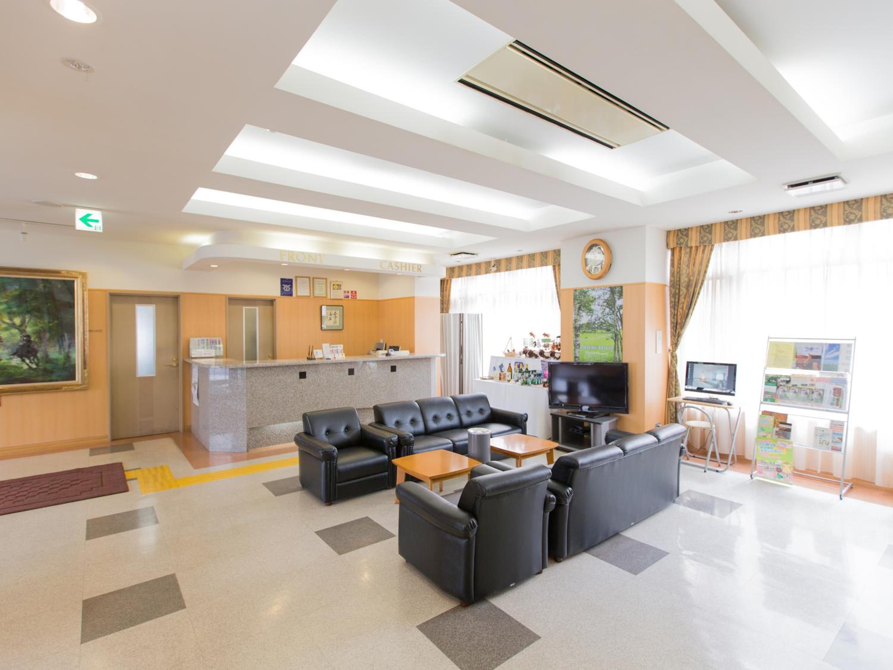 A hotel lobby with a reception desk, seating area, television, and a bulletin board.